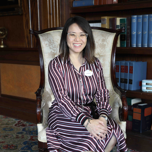 Administration team member seated in a chair with library of books behind her