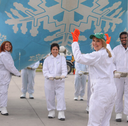 A woman looks back at the camera, her hands are up as she guides a group of Team Members who are piloting a blue balloon with a snowflake design for the Christmas parade.