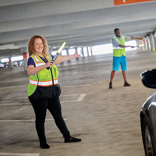 A Parking and Transportation Manager assists her team with parking cars, she is using a light wand to guide a car into a parking spot