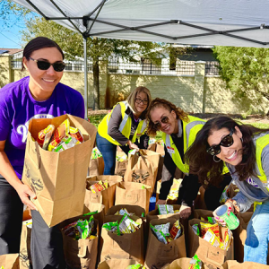 Four Team Members holding brown paper bags of food while volunteering